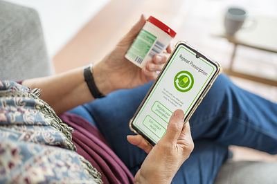A woman requesting a prescription refill on her phone while holding her medication bottle